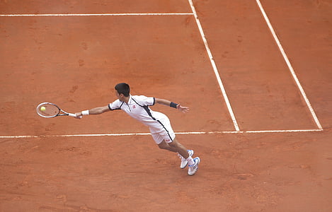 person holding racket smashing racket ball on brown field thumbnail