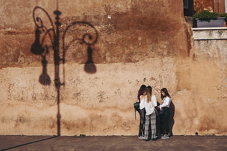 three women having conversation near brown concrete wall at daytime thumbnail