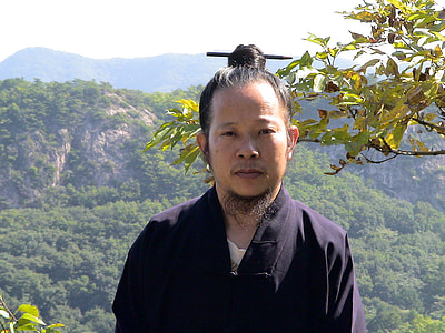 man wearing black v-neck top standing near mountain under cloudy sky thumbnail