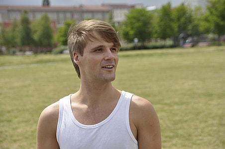smiling man in white tank top standing on green grass field at daytime thumbnail