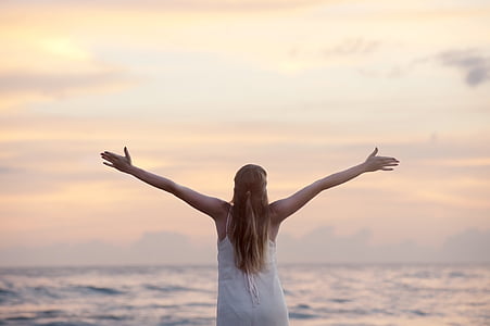 woman raising her hands facing body of water thumbnail