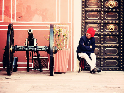 man sitting on chair beside vintage cannon on outdoors thumbnail
