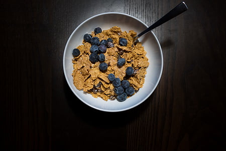 cereals and blueberries on white ceramic bowl with spoon on brown surface thumbnail