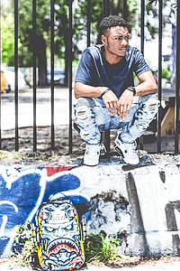 man in black crew-neck t-shirt crouching beside black metal fence during daytime thumbnail