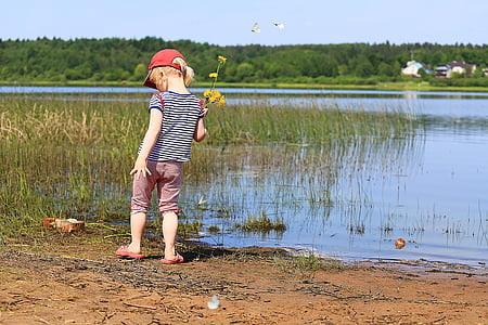 girl holding yellow flowers beside a lake at daytime thumbnail