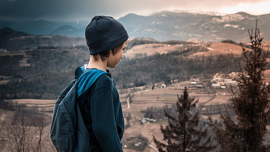 boy wearing blue backpack looking at tree at daytime thumbnail