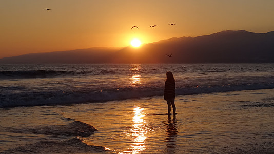 silhouette photo of person standing near body of water during sunset thumbnail