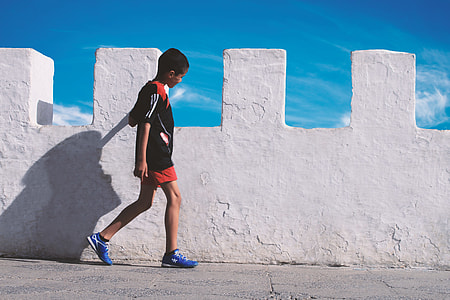 boy walking neat concrete wall during daytime thumbnail