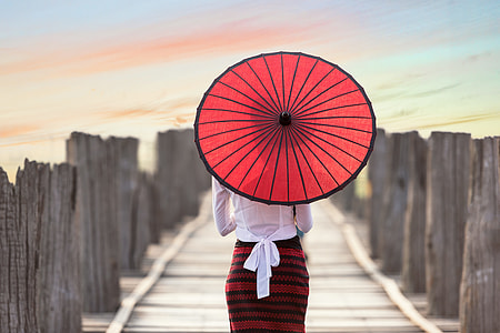 woman in white and red dress using paper umbrella at dock during daytime thumbnail