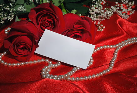 red rose bouquet beside beaded white necklace on red satin textile thumbnail