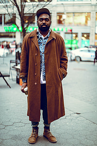 man wearing brown robe standing on gray pavement selective focus photo thumbnail