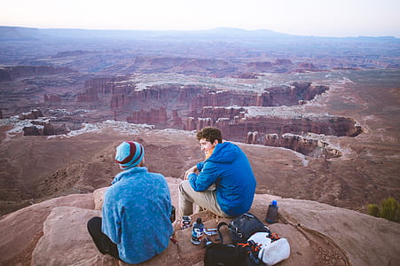 two men eating on cliff during daytime thumbnail