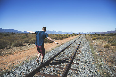 man balancing on train railings under blue sky thumbnail