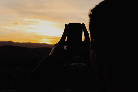 silhouette of person holding phone and taking picture of mountain thumbnail