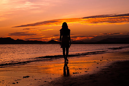silhouette photograph of woman standing near sea shore thumbnail