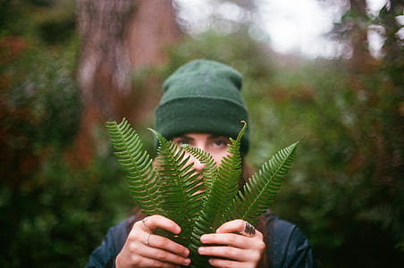 woman wearing green knit cap and black top holding green fern plant in selective focus photography thumbnail