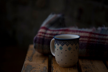 white and blue ceramic mug in front of beige and red textile thumbnail