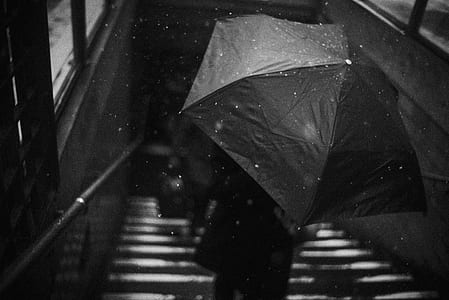 gray scale photo of person holding umbrella on stairs thumbnail