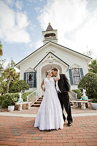 married couple in front of white and brown wooden church on daytime thumbnail