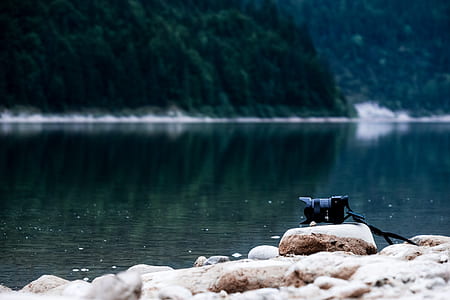 black digital camera on rock facing water at daytime thumbnail