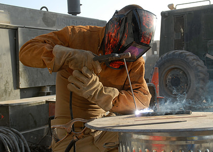photo of person's wearing orange safety gear and black welding helmet thumbnail