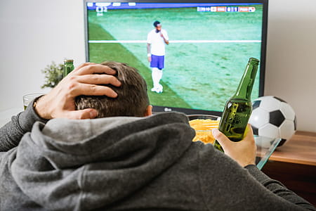 Young man watching football sport on tv at home. thumbnail