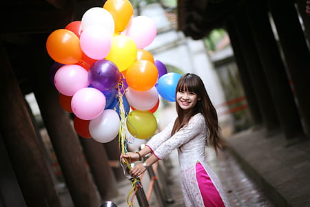 woman in white dress holding assorted-color bundle of balloons thumbnail