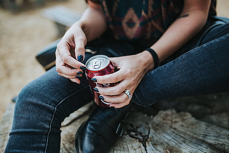 Beautiful blonde woman relaxing with a can of coke on a tree stump by the beach thumbnail
