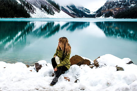 woman sitting on snow near lake thumbnail