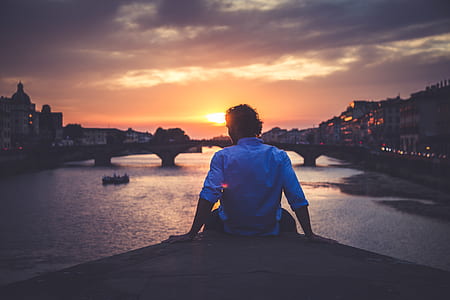 silhouette of man sitting front of bridge during golden hour thumbnail