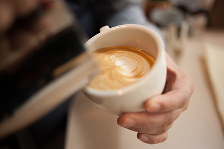 person pouring cream onto white cup with cappuccino selective focus photo thumbnail