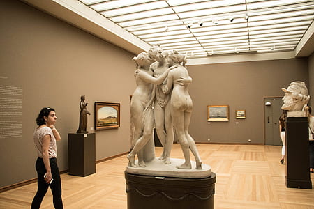 woman standing beside concrete three women statue inside room thumbnail