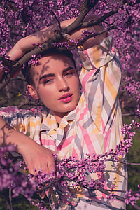 man in white, pink, and yellow striped button-up shirt standing beside tree thumbnail