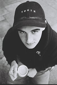 grayscale photography of man with Youth fitted cap holding a cup thumbnail