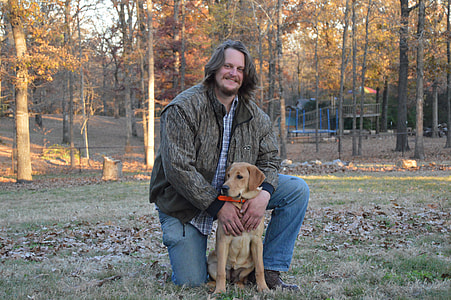 man in grey and black jacket taking photo with brown short coated dog thumbnail