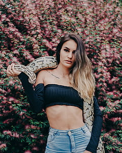 woman with brown snake standing near pink Mimosa flowers thumbnail