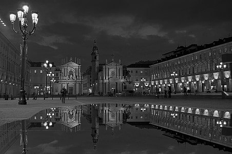 grayscale photo of concrete buildings near body of water and post lamp thumbnail