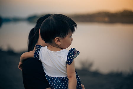 woman carrying a baby near body of water thumbnail