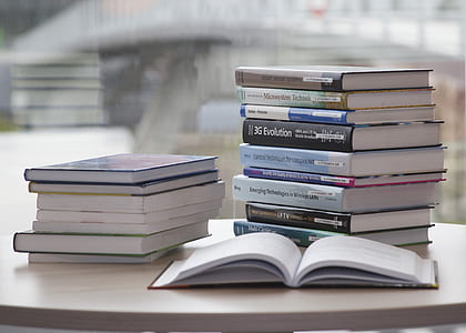 one open book beside pile of books on white table thumbnail