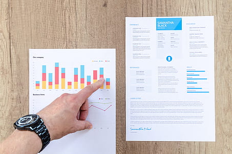 person pointing two white data papers on wood surface thumbnail
