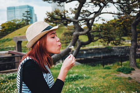 Woman Blowing and Holding White Flower Near Trees thumbnail