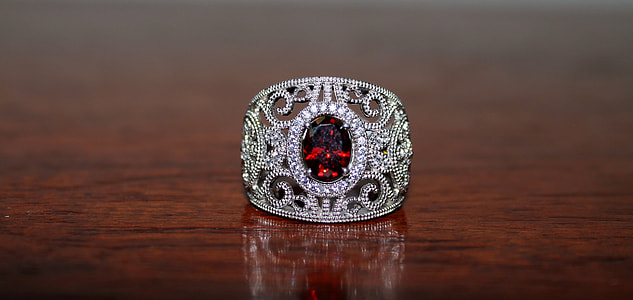 silver-colored ring with red gemstone on brown wooden surface thumbnail