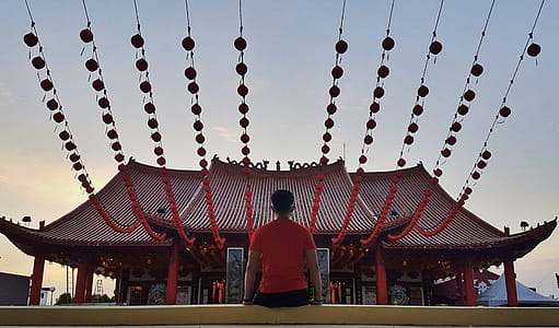 Man Sitting on Yellow Concrete Pavement Infront of Red Pagoda thumbnail