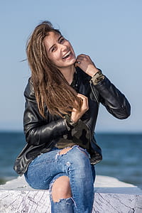 smiling woman wearing black jacket sitting on grey slab thumbnail