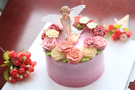 pink icing covered cake on table with fairy figurine thumbnail