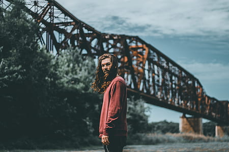 man standing near tall trees and metal bridge during daytime thumbnail