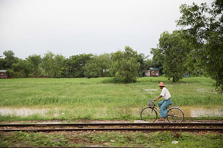 A man riding a bicycle near train tracks with paddy field in the background thumbnail