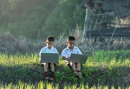 two boys in white dress shirt sitting on grass using laptop computers thumbnail