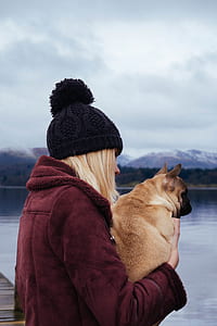 woman carrying brown dog beside body of water thumbnail