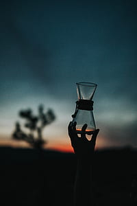 silhouette photo of left human hand holding clear glass container thumbnail